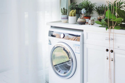 A white dryer with white curtains in the background to illustrate if grounding sheets can go in the dryer