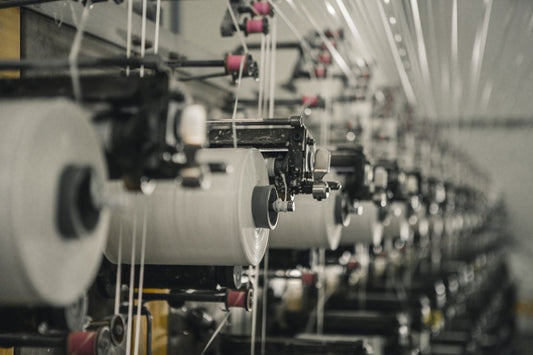 Close-up of textile machinery with large spools of white thread in an industrial factory.