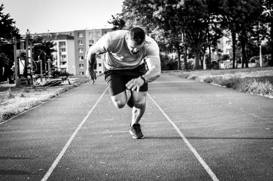 Black-and-white photo of a male athlete sprinting on an outdoor track, emphasizing strength and focus.