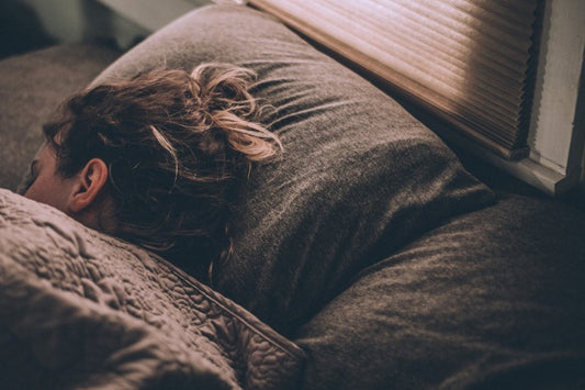 Person sleeping peacefully in a cozy bed with dark bedding near a window with closed blinds.