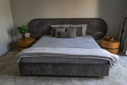 Modern bedroom with a neatly made bed featuring gray bedding, pillows, and side tables with decor accents.