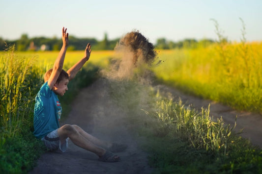 Child playing in the dirt on a country path, throwing soil into the air, symbolizing a natural connection to the earth.
