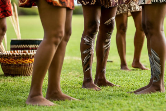 Close-up of bare feet and legs with traditional body paint during a cultural ceremony on grass.