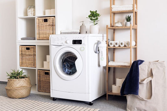 Minimalist laundry room featuring a front-loading washer, grounding sheet filter attachment, and neatly organized shelves with towels and baskets.